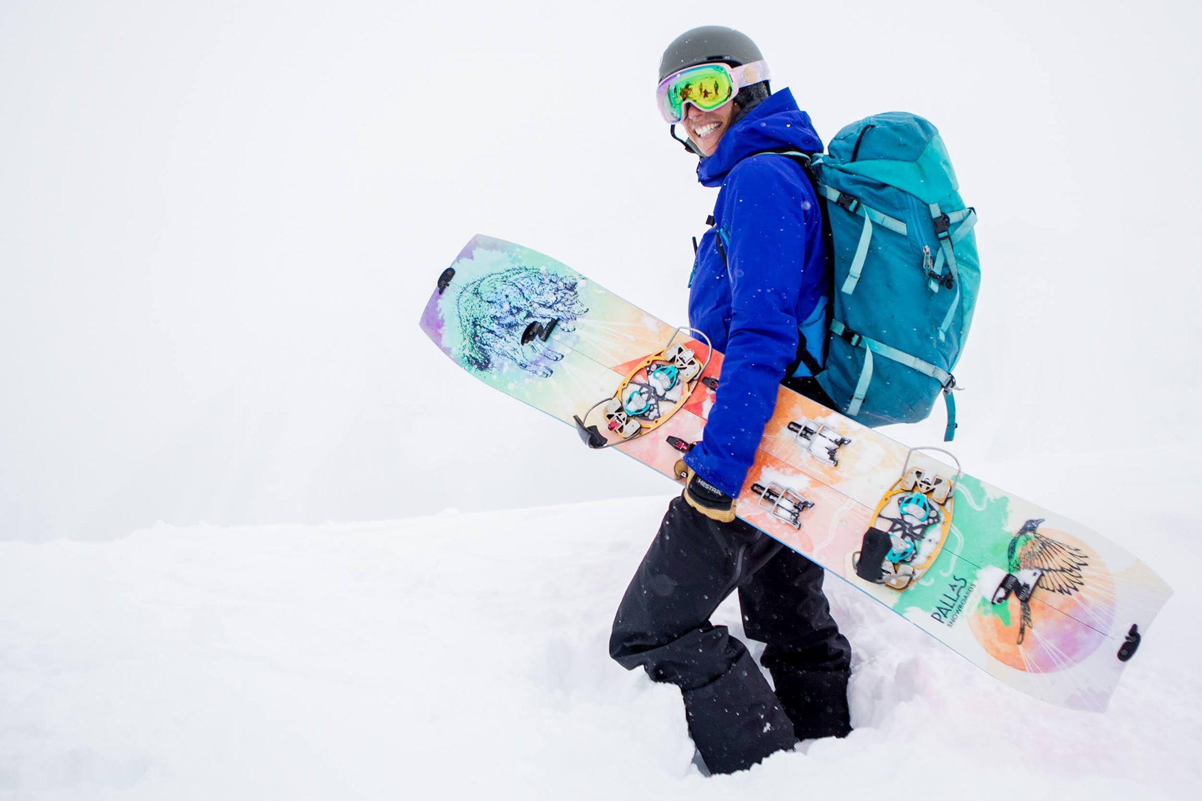 A female splitboarder stands in the snow holding a Pallas Epiphany splitboard that's mounted with a hardboot binding system. 